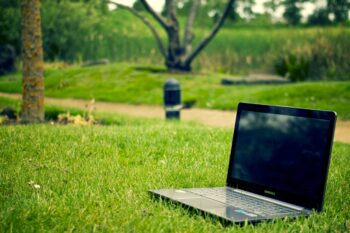 Photo is of an open laptop sitting on grass in a park. 
