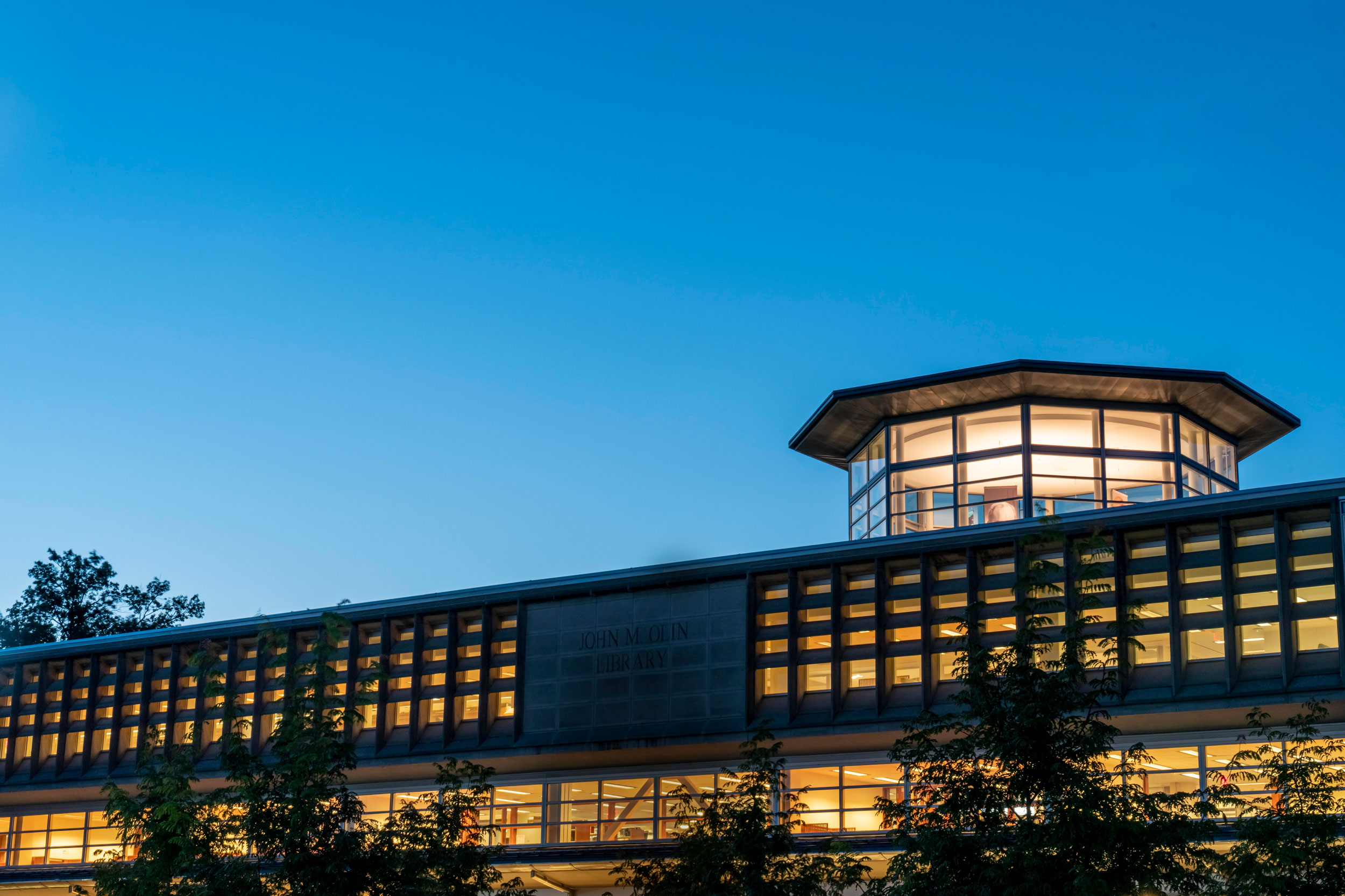An exterior photo of the lights on inside Olin Library at dusk.
