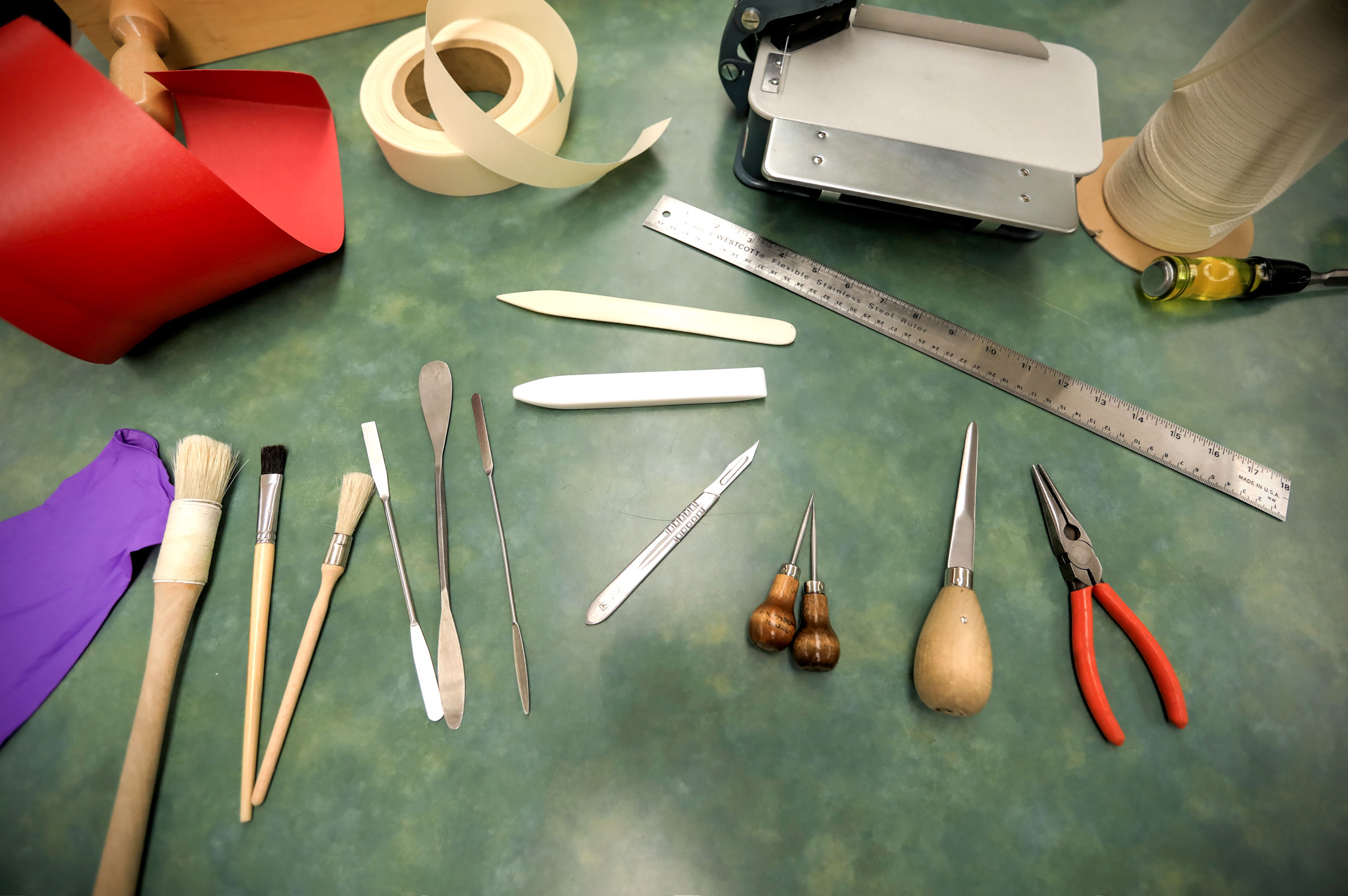 Tools used within the Preservation Lab. There is book tape, a metal ruler, pliers, paint brushes, gloves, spatulas, an exacto knife, chalk, and more.