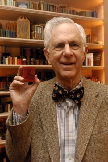 Julian Edison holding up a miniature book in front of a bookshelf of his miniature book collection. 