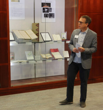 Special Collections Curator Joel Minor presenting in front of the "Connecting Contexts" exhibition, which is behind glass. 