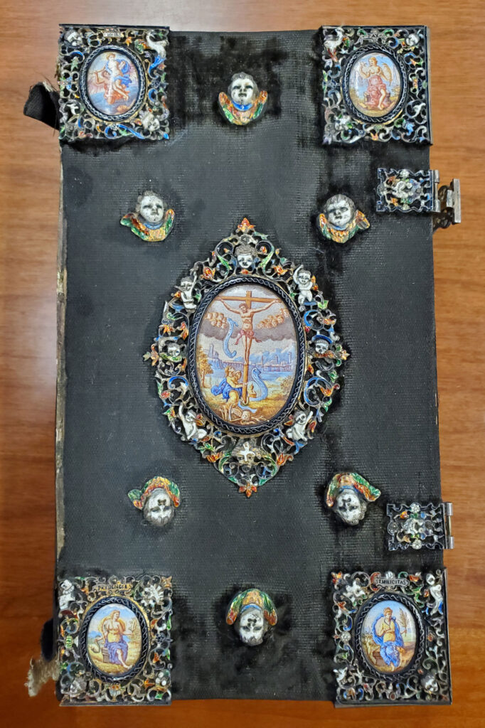 The book has what may be brooches attached to the front cover in decoration. There are six, small cherubs arranged on the cover, along with four small paintings of stories within the Psalms at each corner of the cover. At the center of the book cover is a larger, intricate drawing of Jesus on the cross.