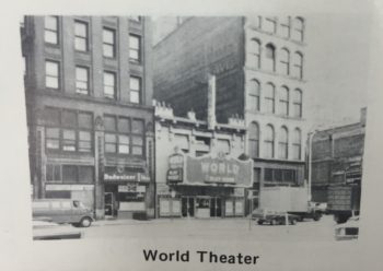 A small but prominent building with a sign declaring it the "World Theater" between two five-story or more buildings. 