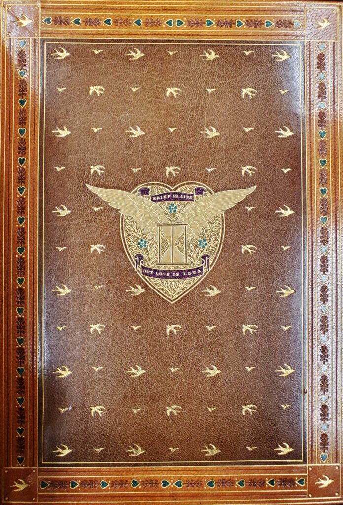 This endpaper for The Princess is one of two and has outlines of swallows in flight stamped throughout the leather. In the center of the endpaper is a seal with an hourglass surrounded by wings and blue flowers at its center; the seal has banners above and below the hour glass that read "Brief is life but love is long."