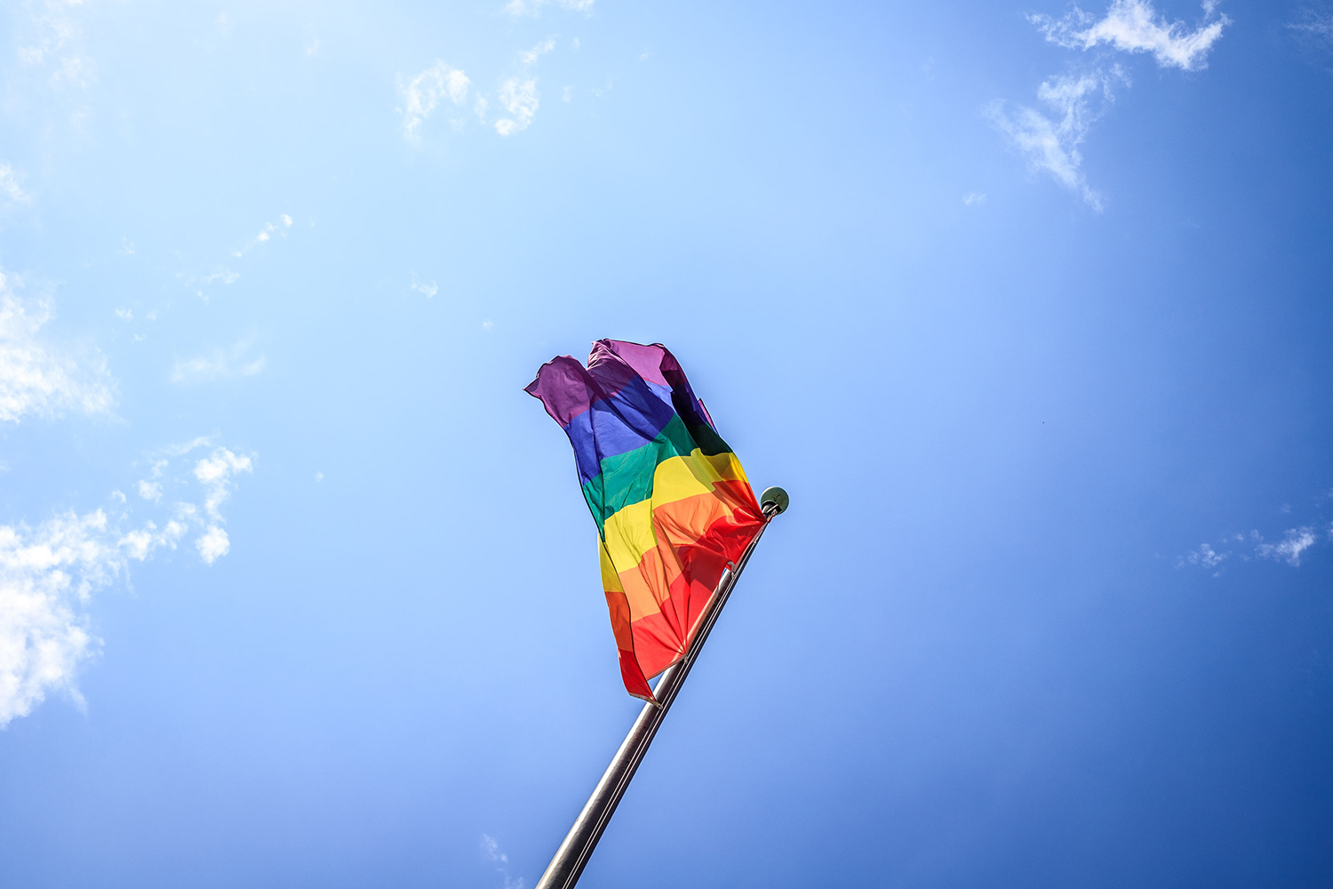 Rainbow pride flag being flown against the background of a crisp blue sky.
