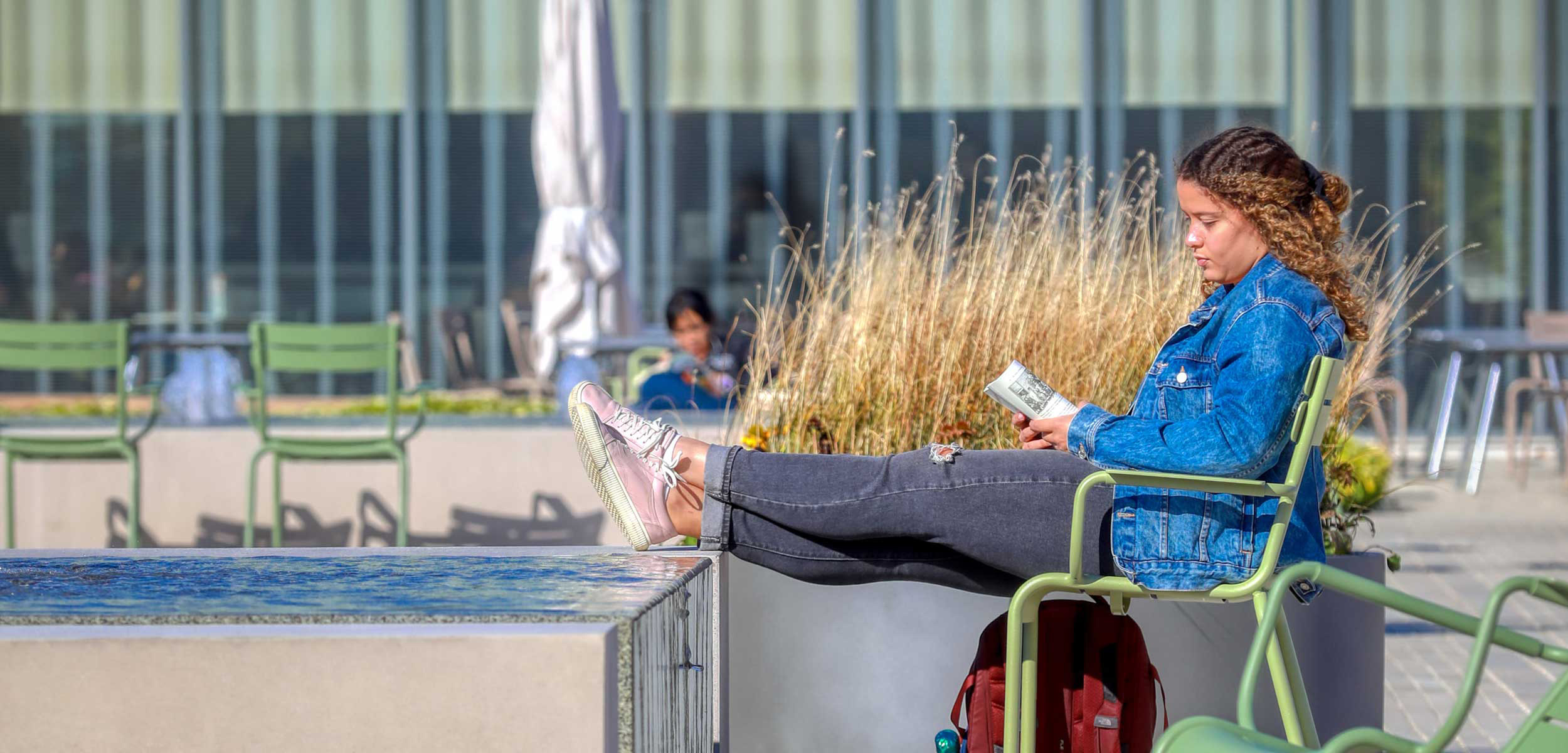 Student sitting outside on campus reading a book with their feet propped up.