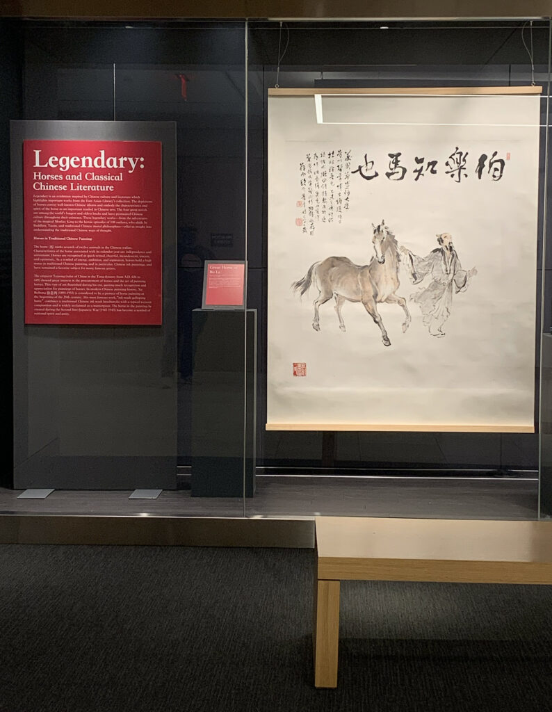 The image shows the placard for Legendary: Horses and Classical Chinese Literature exhibition in Olin Library's Thomas Gallery. Alongside the plaque is a traditional Chinese painting of a man and an unsaddled horse.