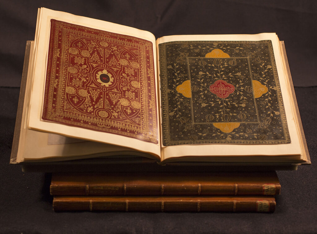 Intricately decorated leather covers of books pressed into sheets of a larger scrapbook that sits open atop two additional scrapbooks.