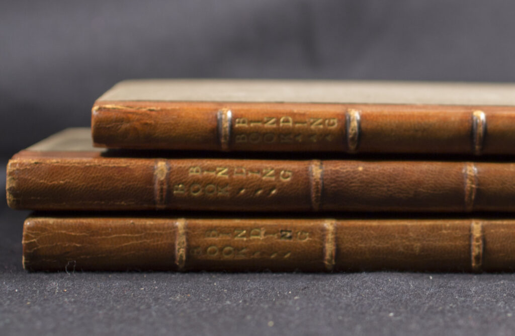 Three thin, leather bound books with the titles - all are volumes of Book Binding - imprinted horizontally.