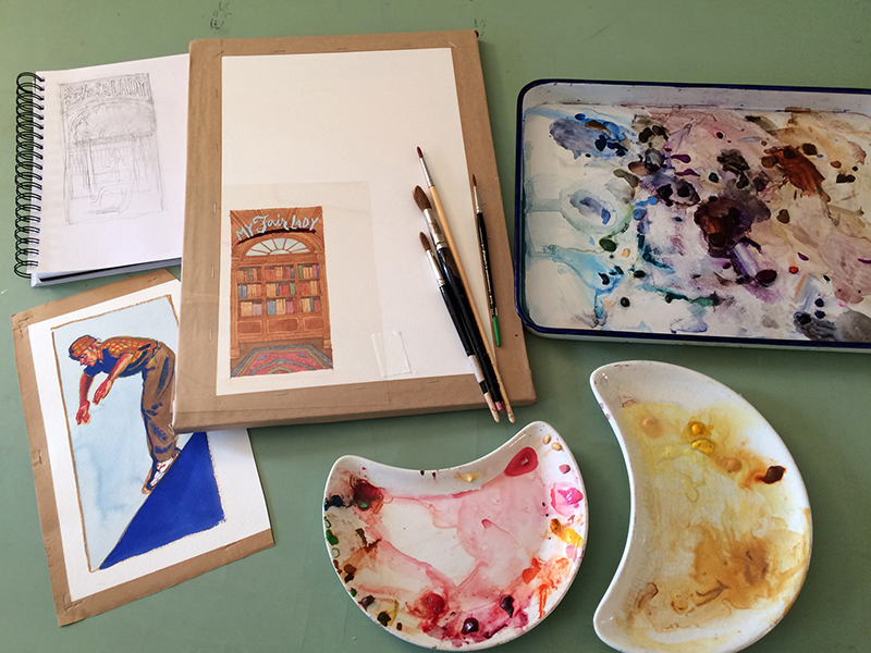 The image shows three paint palettes of different shapes with watercolors of different color families in each. Alongside the paint palettes are a spiral ringed sketch book, a finished watercolor painting, and a painting in-progress with five fine-tipped paint brushes laid atop it.