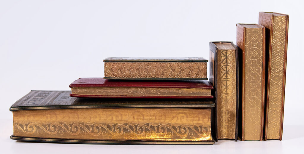 Six books of various sizes displayed spine-in so that the gold edges and the geometrical designs etched into them are on display.