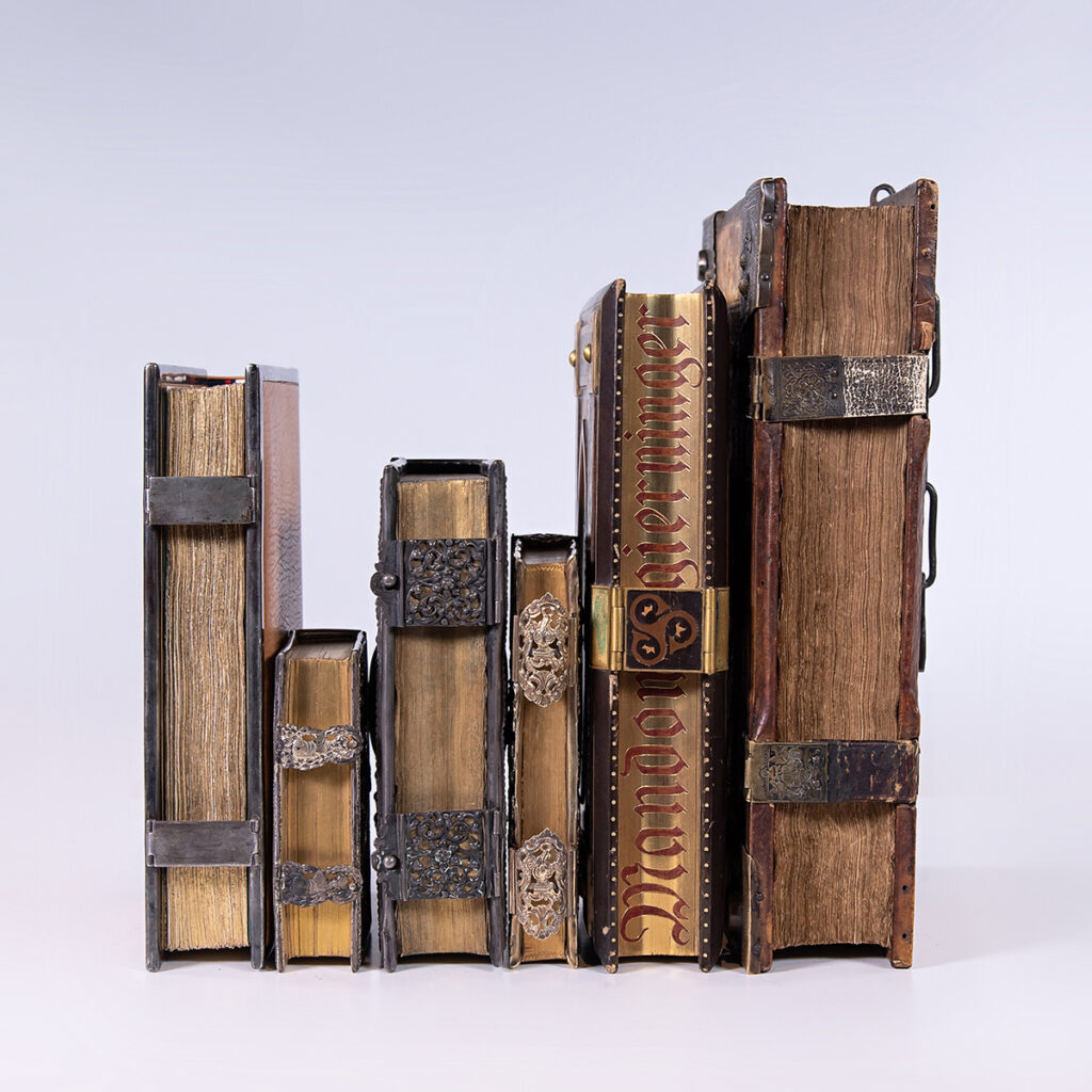 Six books lined pages out so that the image captures the locks attached to the bindings of each along with the gold along the pages of some.