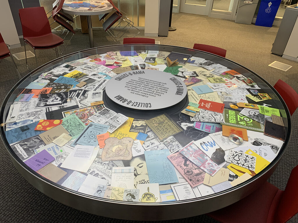 A circular table with hundreds of zine booklets displayed under a glass case.