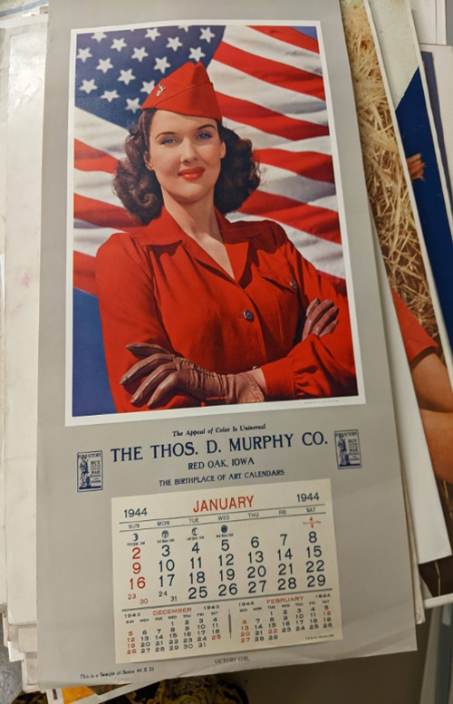 A full-color, half-page width Victory Girl Calendar spread. A red-lipsticked woman wearing a bright red blazer stands arms crossed in front of the United States flag with a small calendar for January 1944 printed at the bottom.