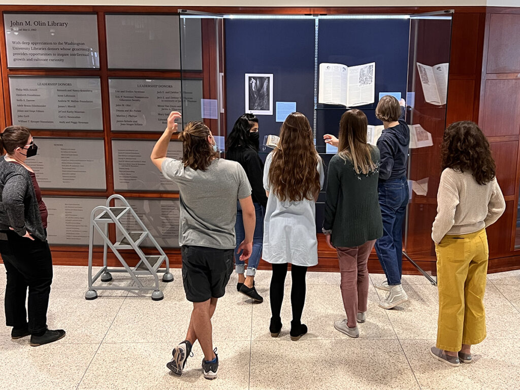 Students discussing exhibition material placement in front of an open, floor-to-ceiling exhibitions display case.