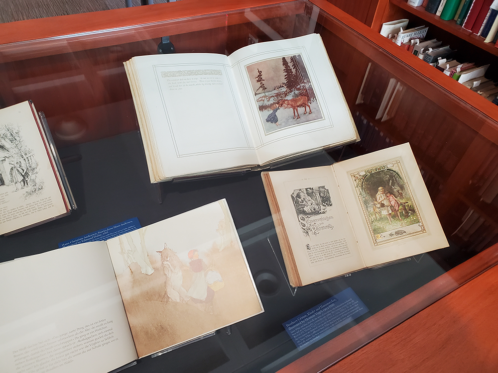 Four fairytale books open to display colorful illustrations on display under a glass case.