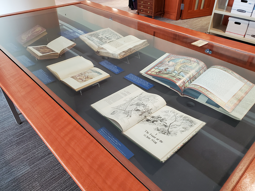 Six fairytale books, some shown open to colorful illustrations, on display in a glass case.