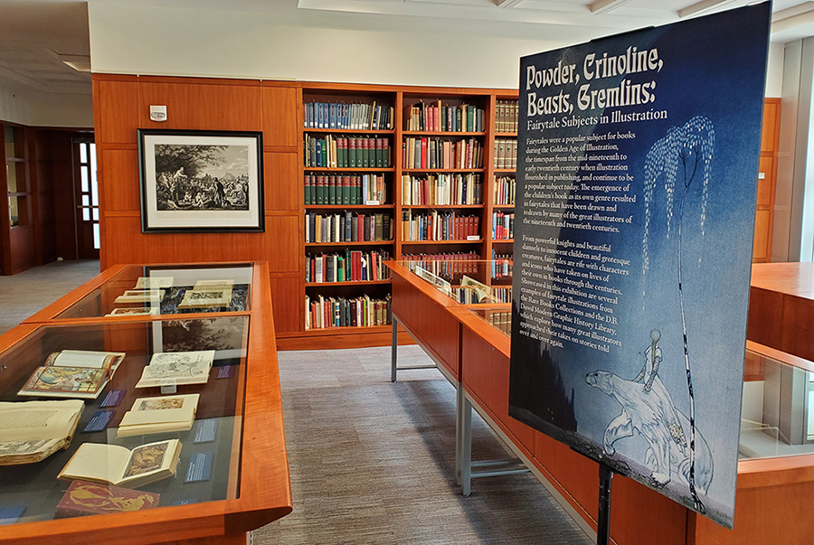 The books for the exhibition on display in glass cases with a banner alongside the case with the exhibition name and details in smaller print.