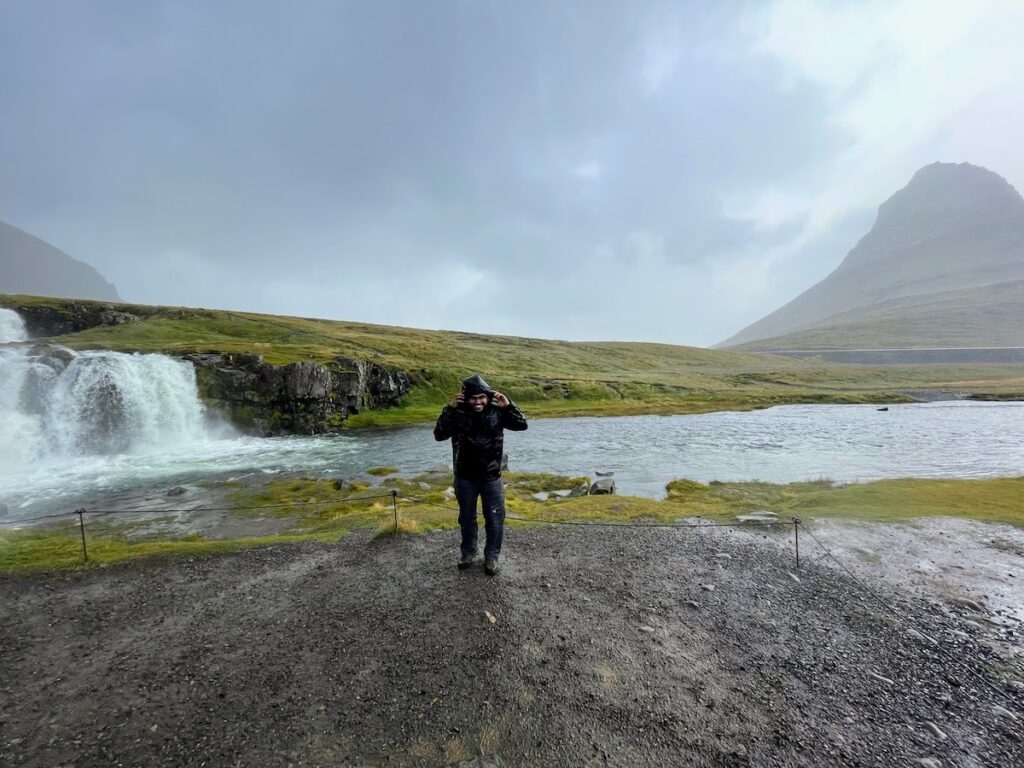 Man in front of a windswept landcsape with water falling into a stream.