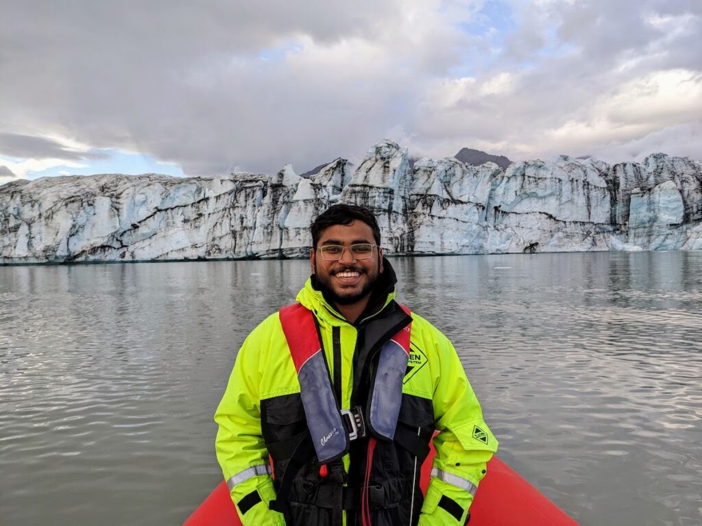 Man on a boat in a lagoon with icy glaciers in the background.