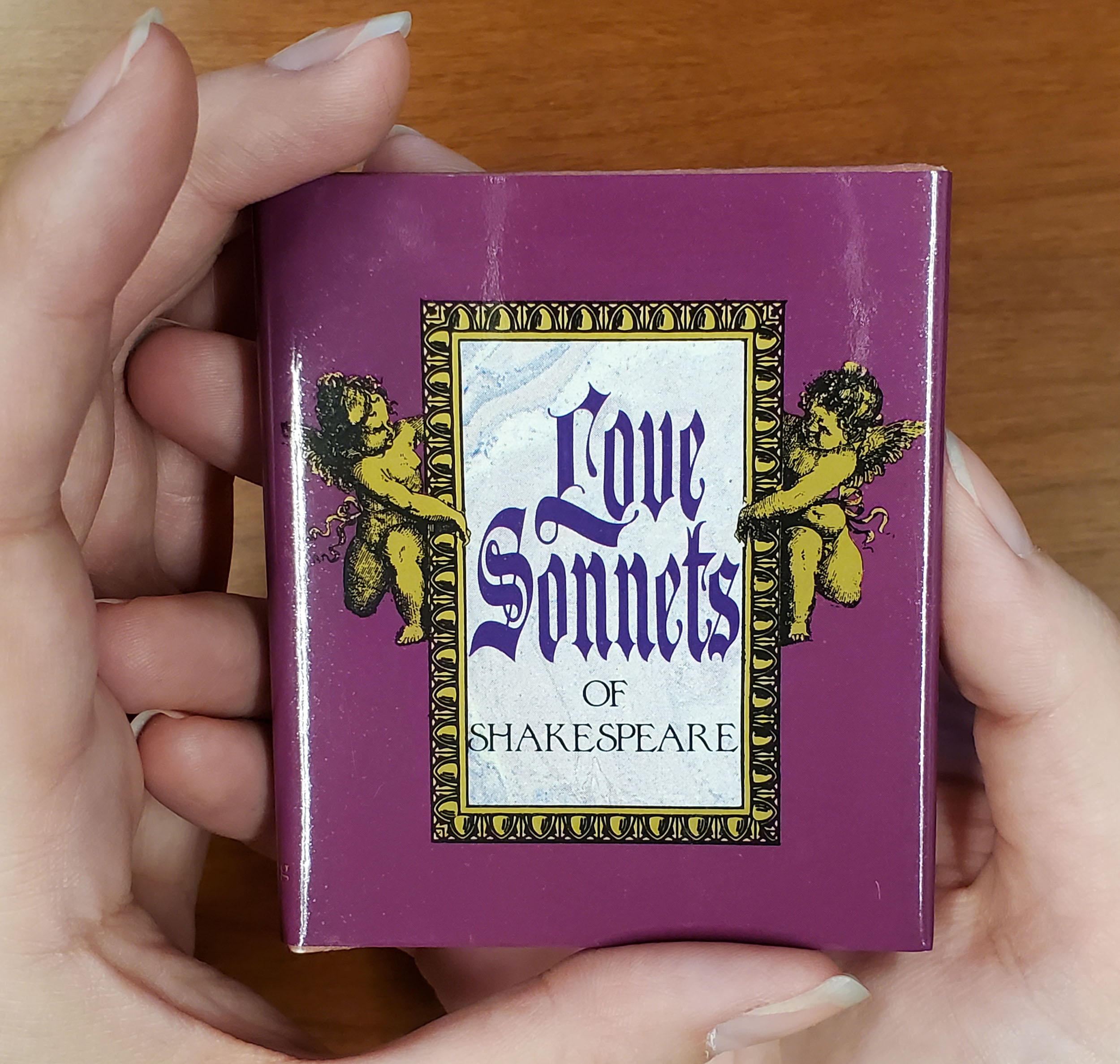A miniature book titled Love Sonnets of Shakespeare held in the palm of someone's hand.