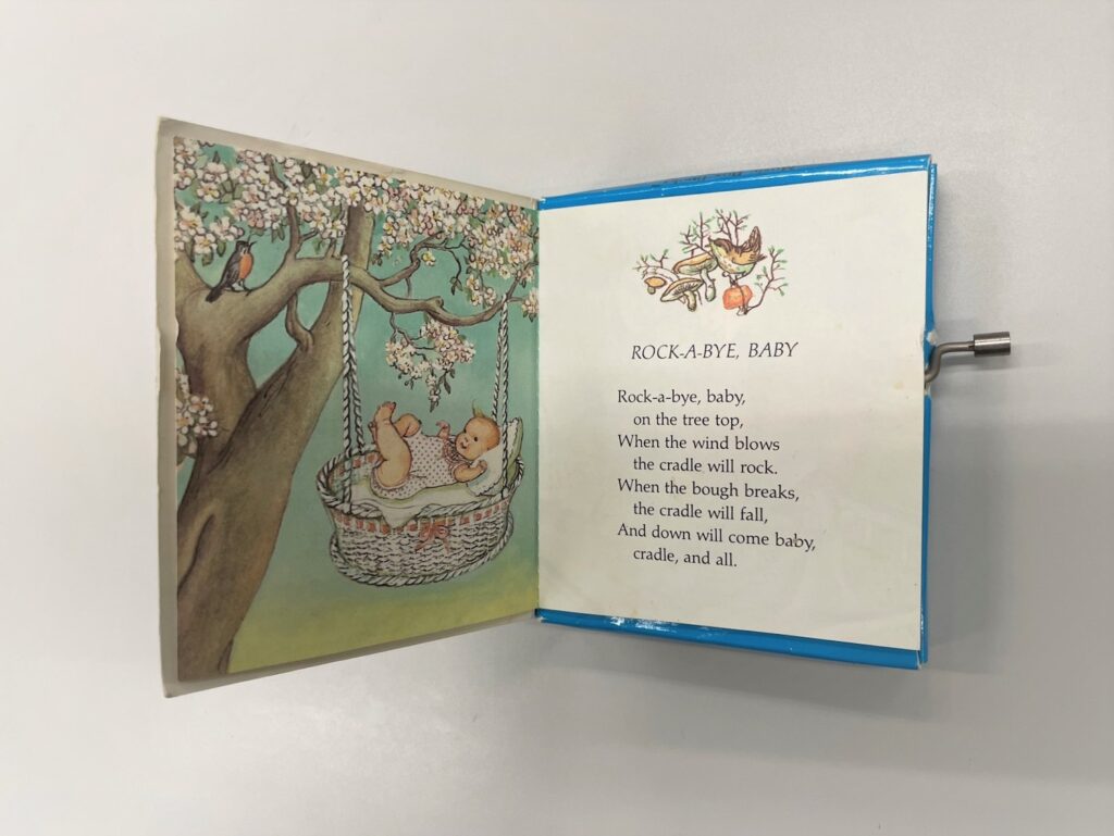 Cradle with baby hanging from a branch of a flowering tree with the song Rock-A-Bye-Baby on the following page.