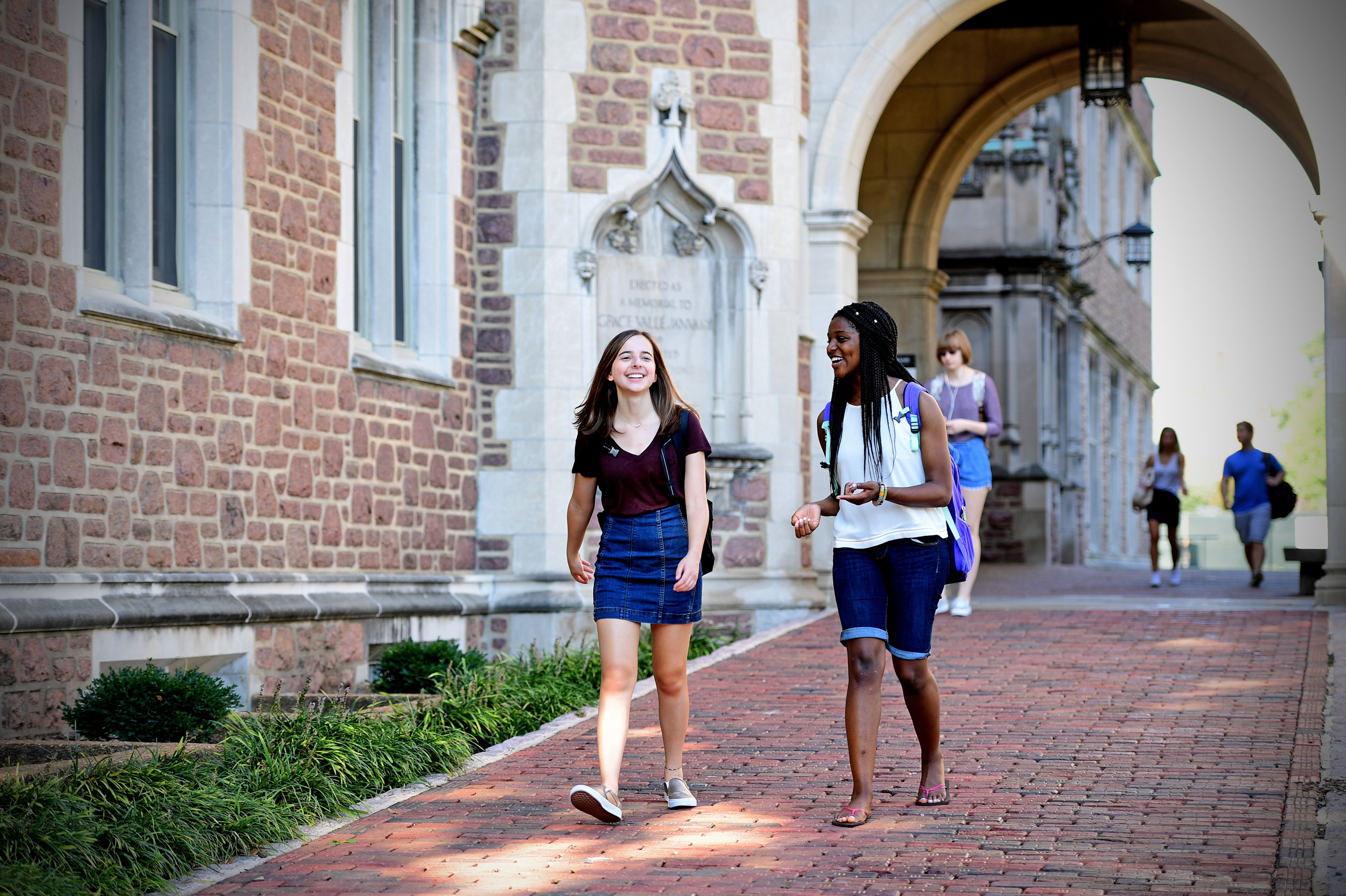 Two students walking on a campus path while chatting.