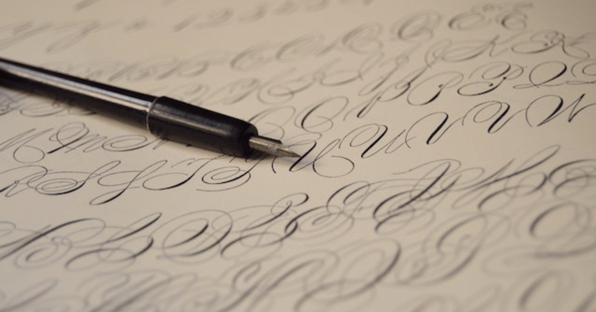 A calligraphy pen resting on top of a sheet of paper with the alphabet written out.