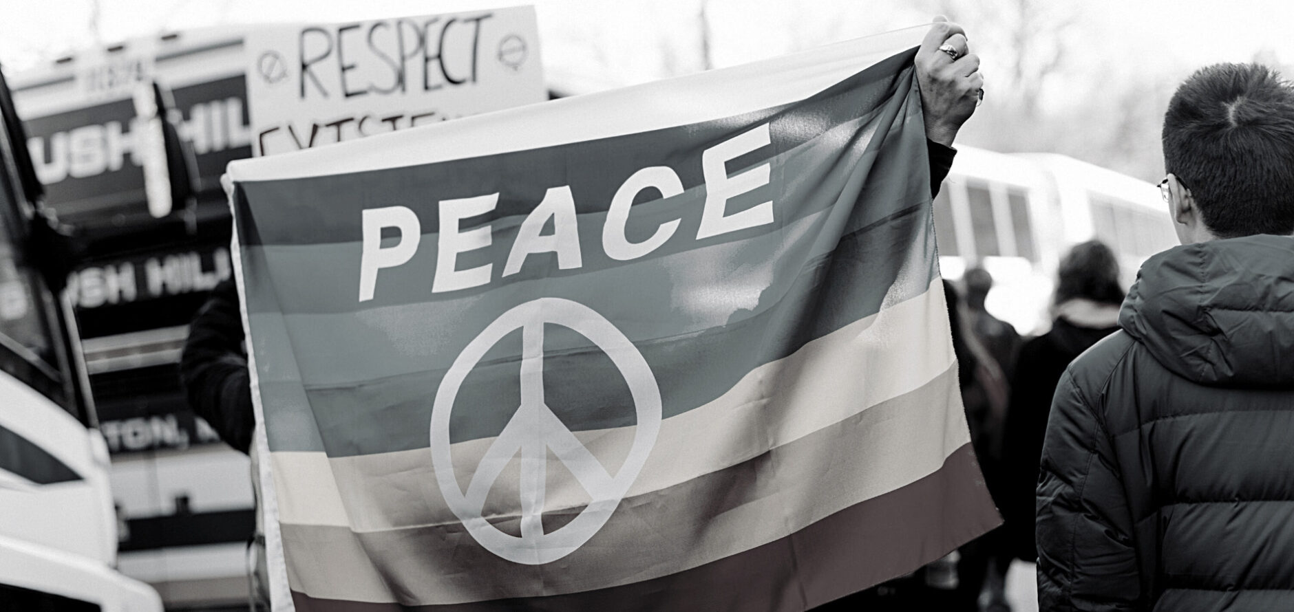 A black-and-white photo of a person holding a peace flag over their body.