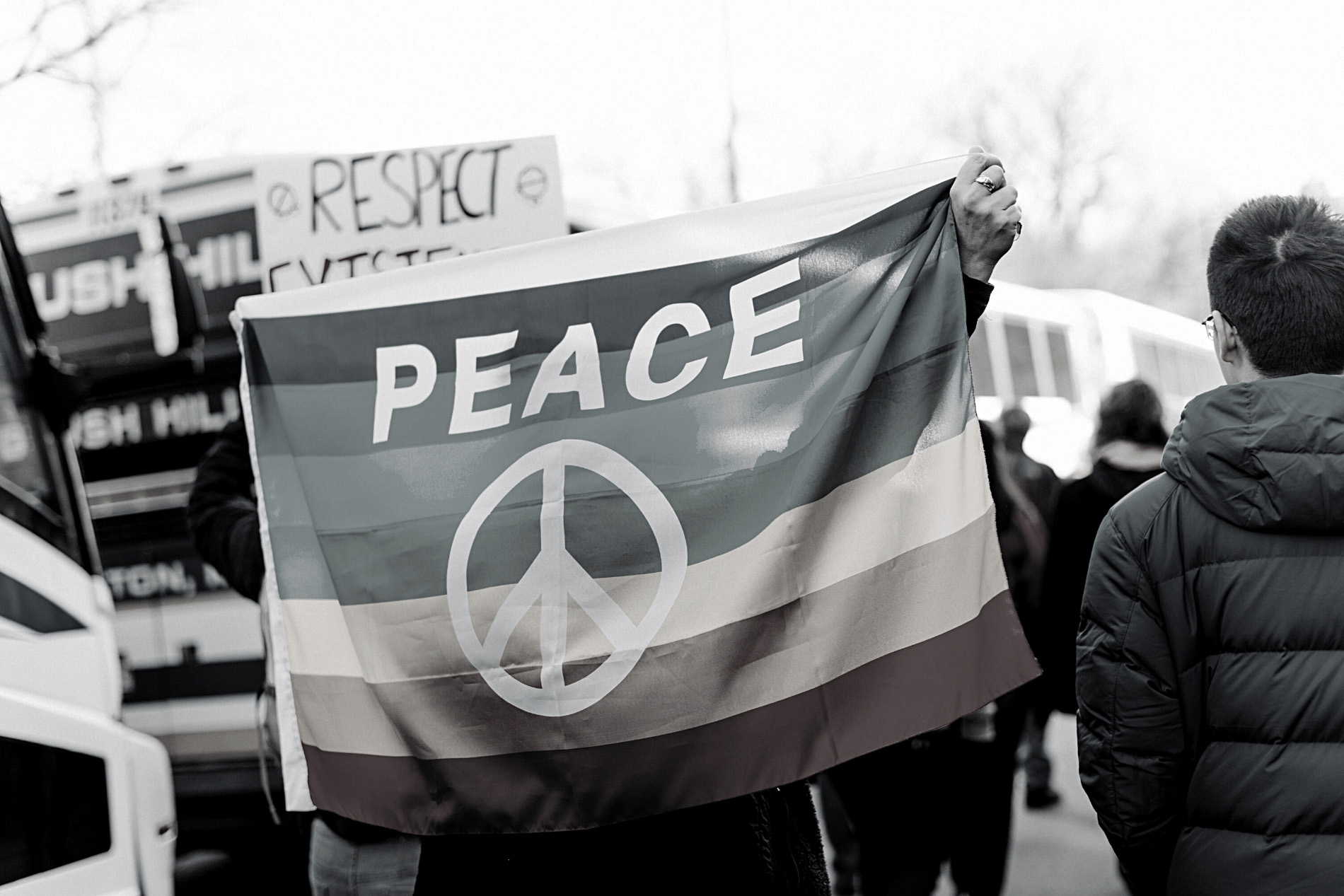 A black-and-white photo of a person holding a peace flag over their body.