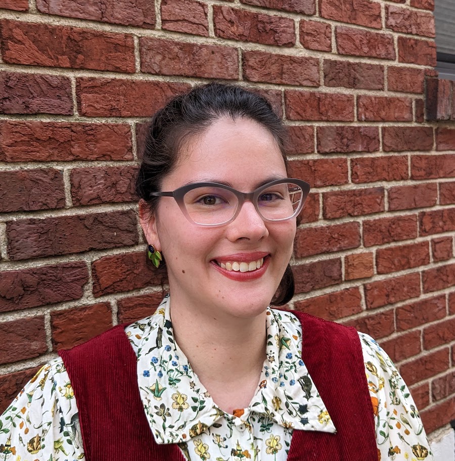 Bespectacled smiling woman in front of a red brick wall.
