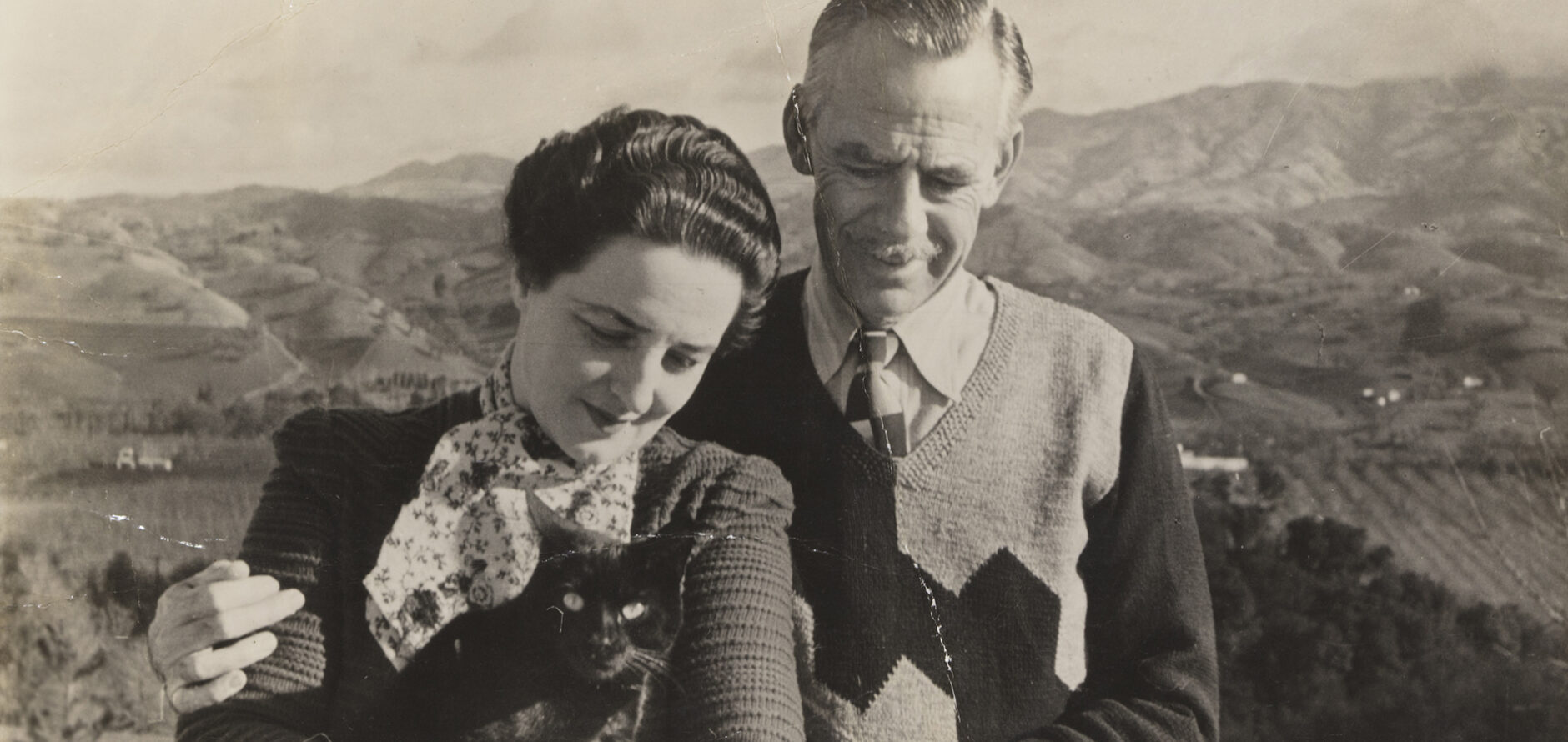 Carlotta and Eugene O'Neill with their black cat Puss circa 1940 standing outside the Tao House in Danville, California, with the mountains in the background.