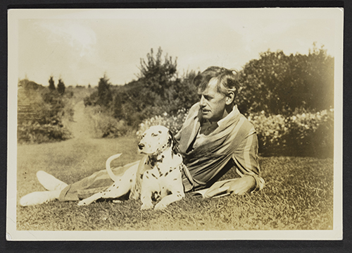 Playwright Eugene O'Neill is laying on the ground in a field with his Dalmatian, Blemie.