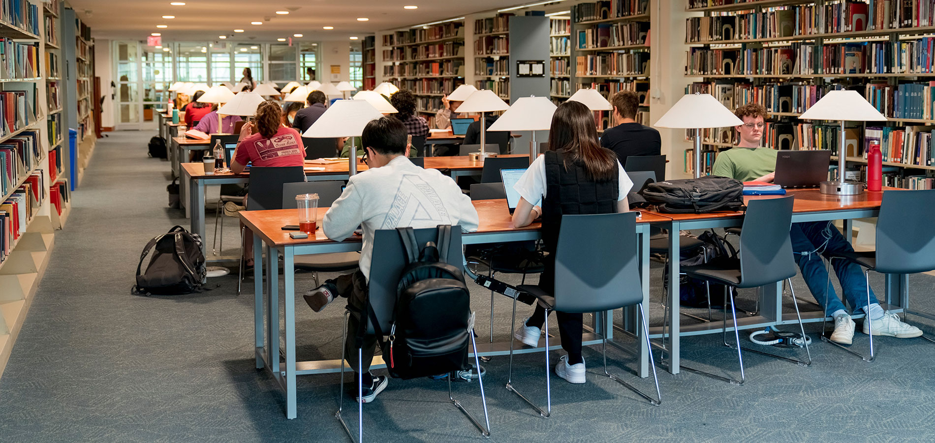 Students studying on their laptops at long desks in Olin Library with bookshelves on both sides.