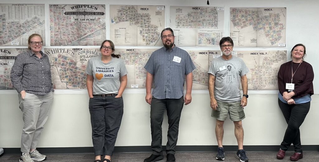 5 individuals standing in front of two rows of color coded maps.