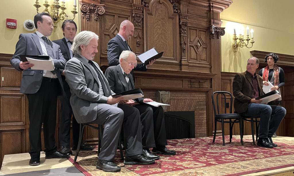 A group of seated people reading on stage