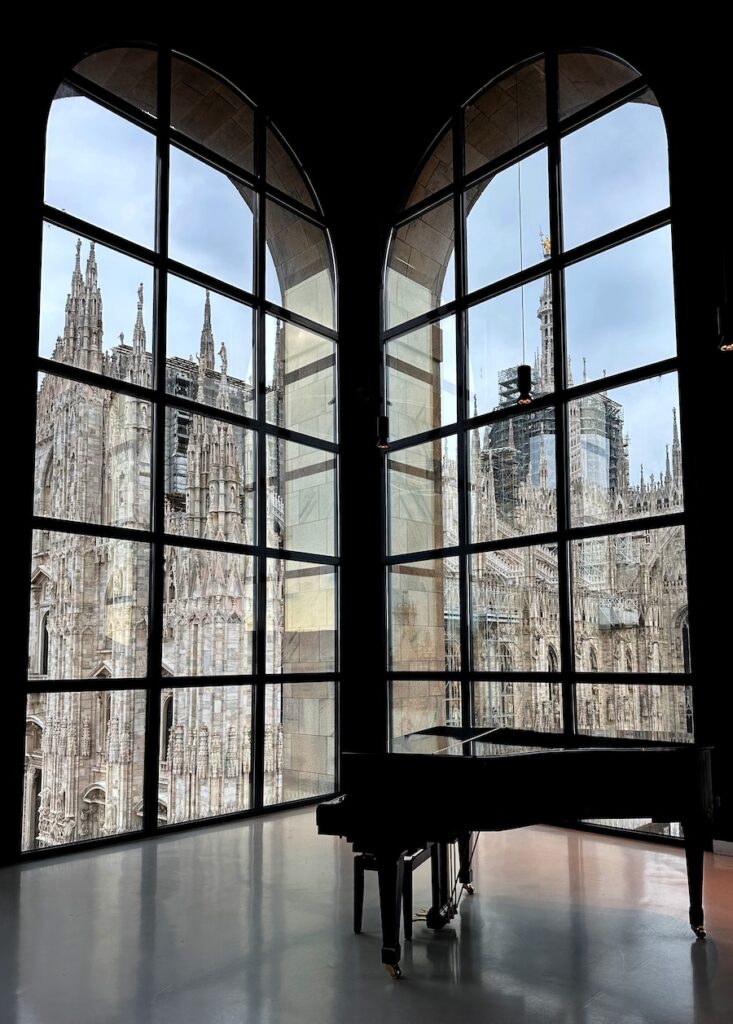 A piano in a room with tall glass windows reflecting monuments outside.