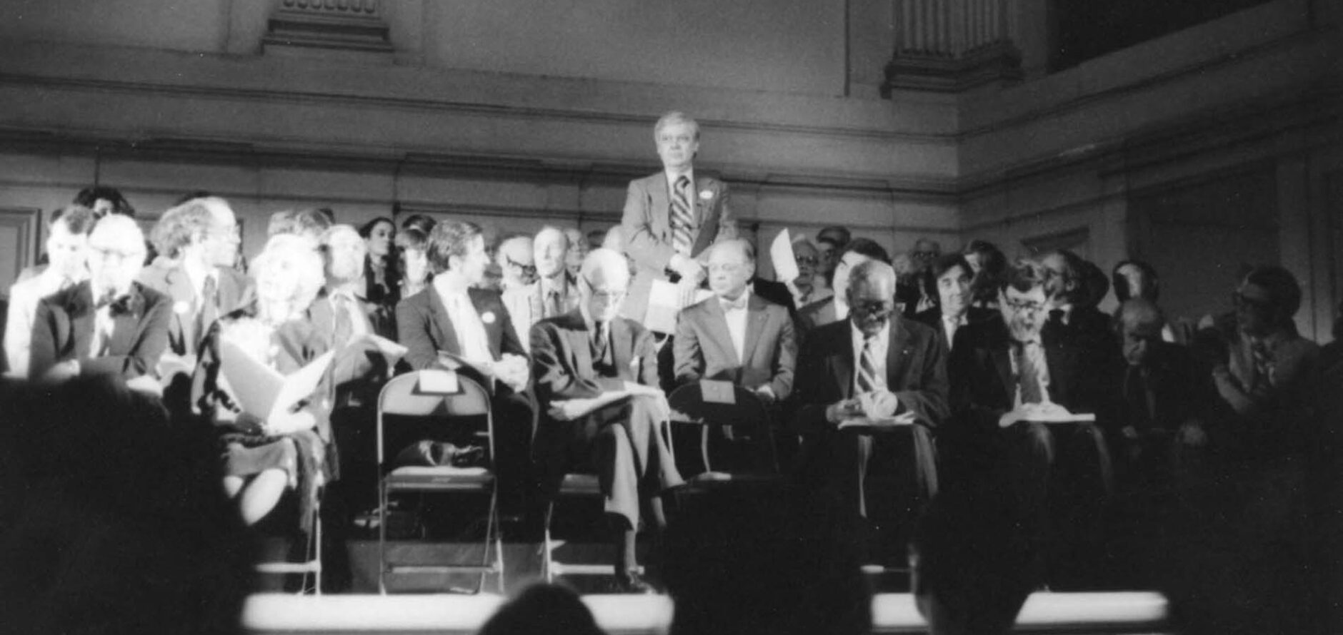 William H. Gass standing amongst a seated crowd.