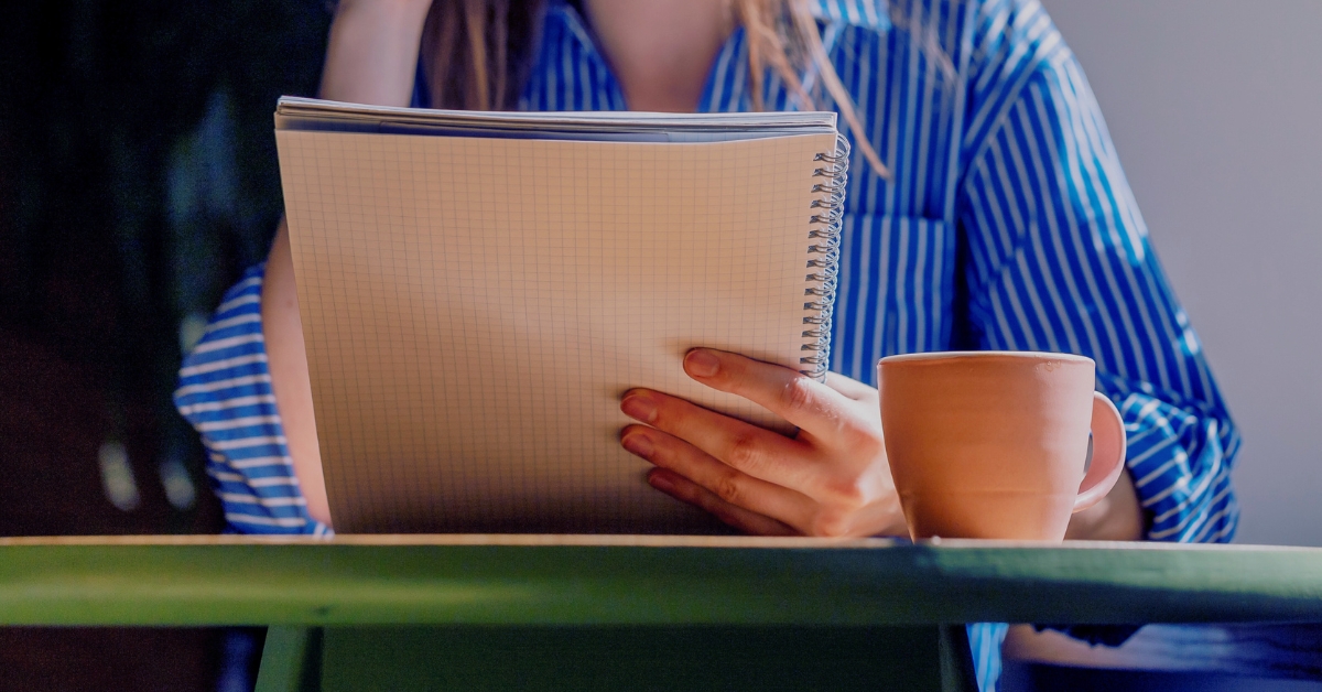 Closeup of a person holding notebook,reading syllabus in cafe with coffee cup on table⁠