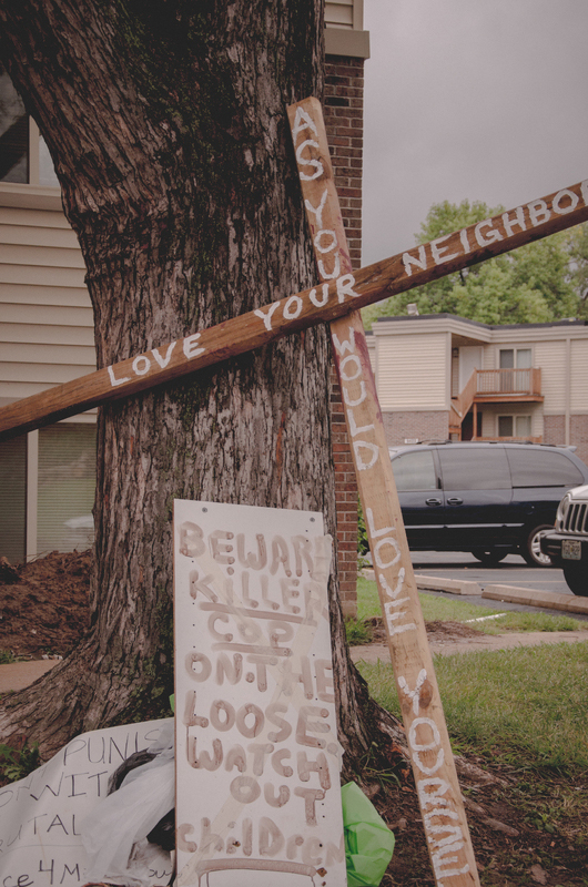 A cross and signs leaned against a tree.