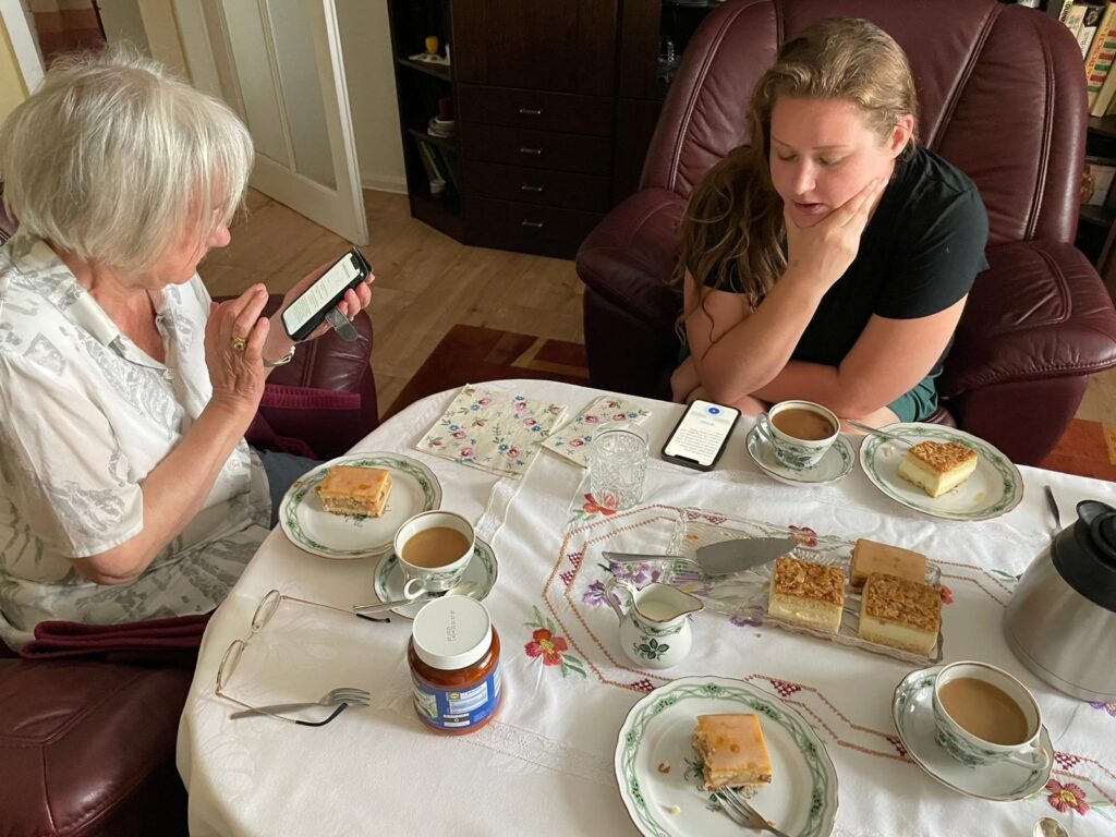 Two people at a dining table with tea and cakes.