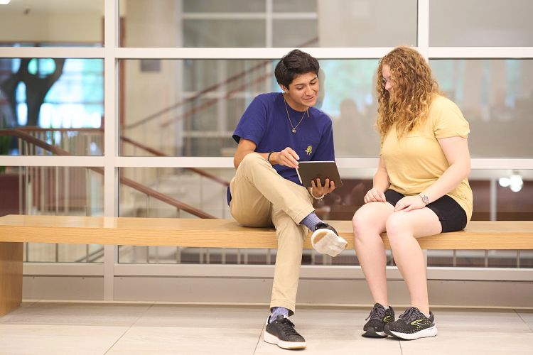 One student helps another on a bench in the main hallway of Olin Library.