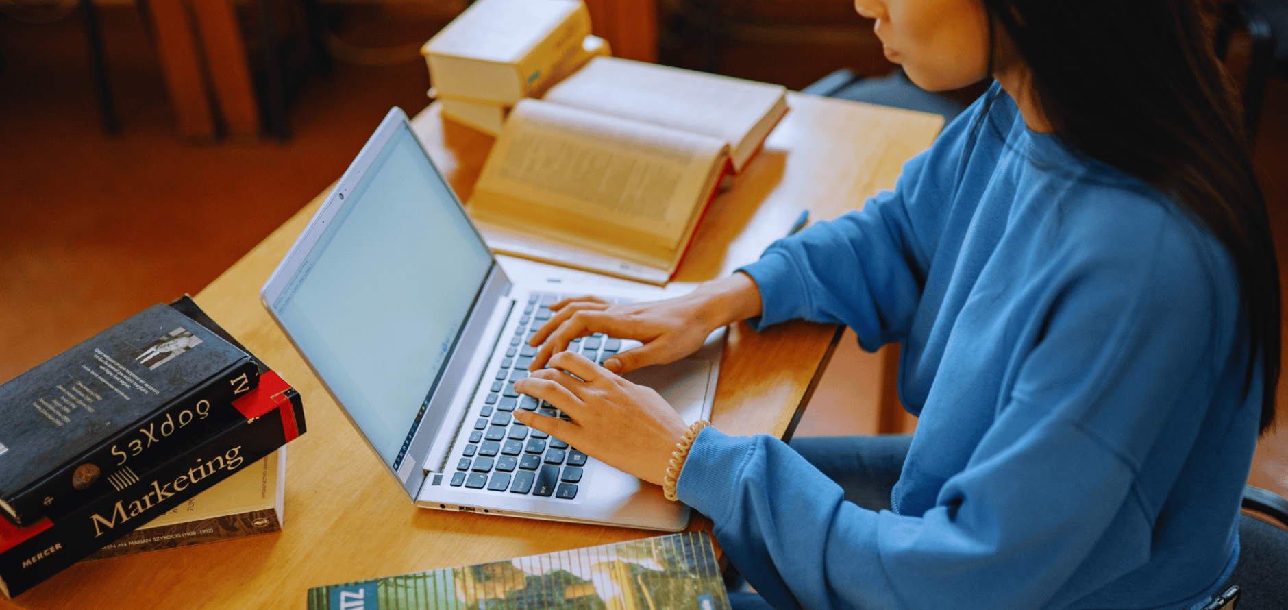 Stock photo of student typing on laptop with stack of books