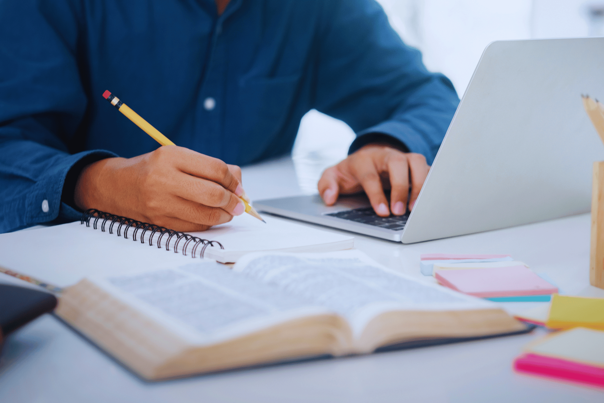 Stock image of person taking notes in notebook and scrolling on laptop